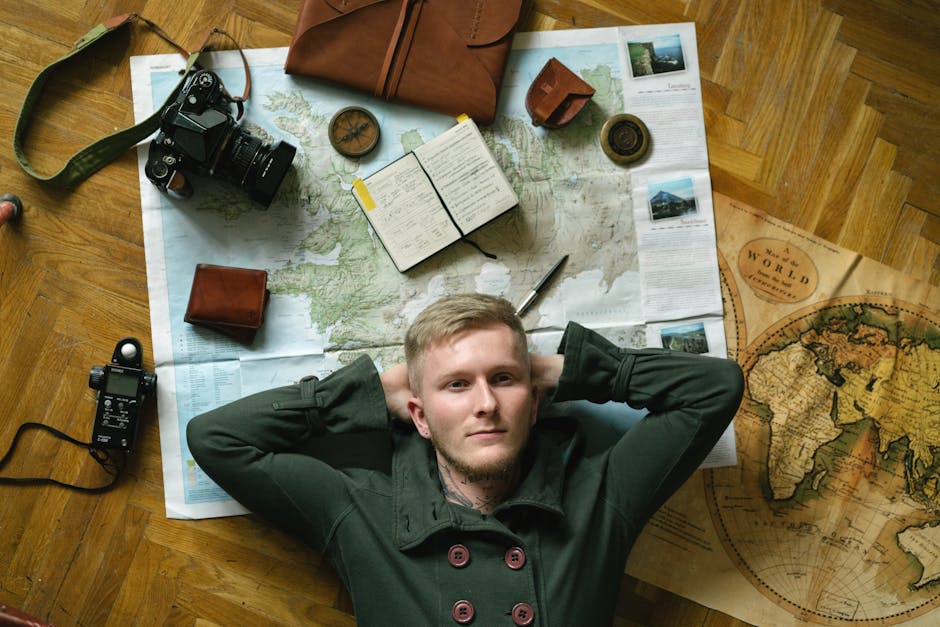 Young man dreams of travel, surrounded by maps, camera, and notebook.