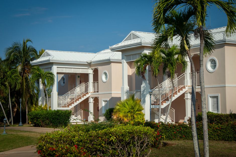 Exterior view of a tropical resort with classic architecture and lush palm trees under a clear blue sky.