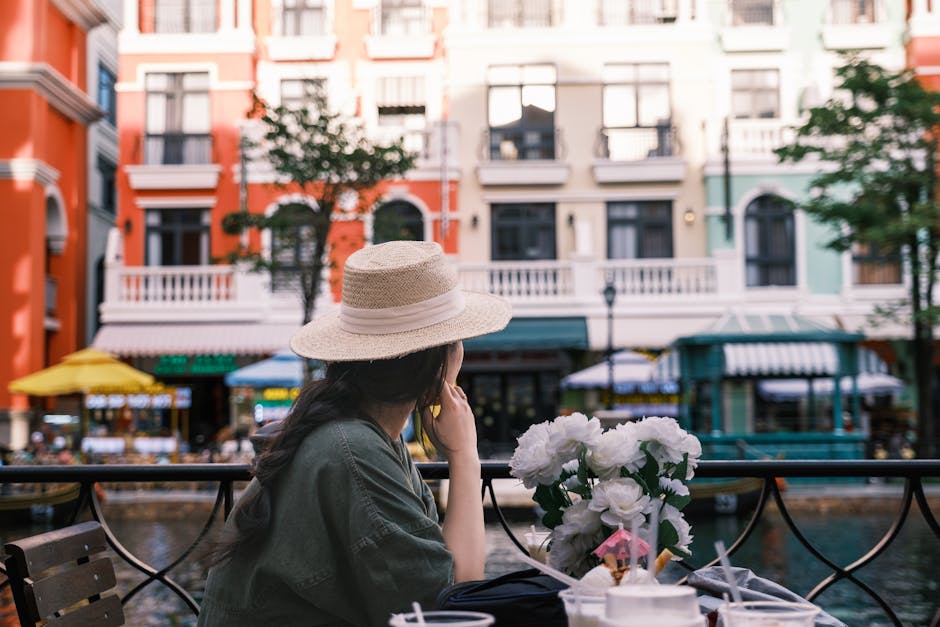 Woman at an outdoor cafe enjoying a view of colorful buildings in a lively street setting.