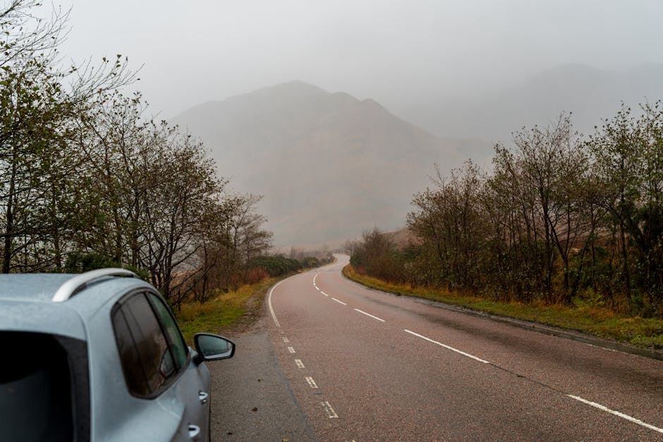A misty mountain road scene with a distant car and autumn foliage in a tranquil landscape.