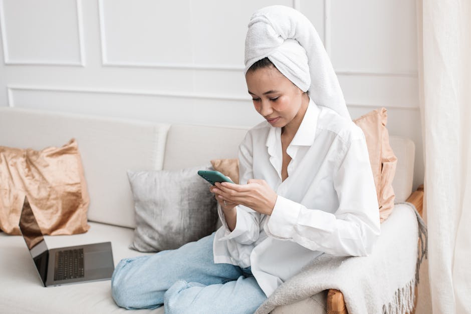 Young woman sitting on sofa with smartphone and laptop, enjoying a relaxing moment at home.