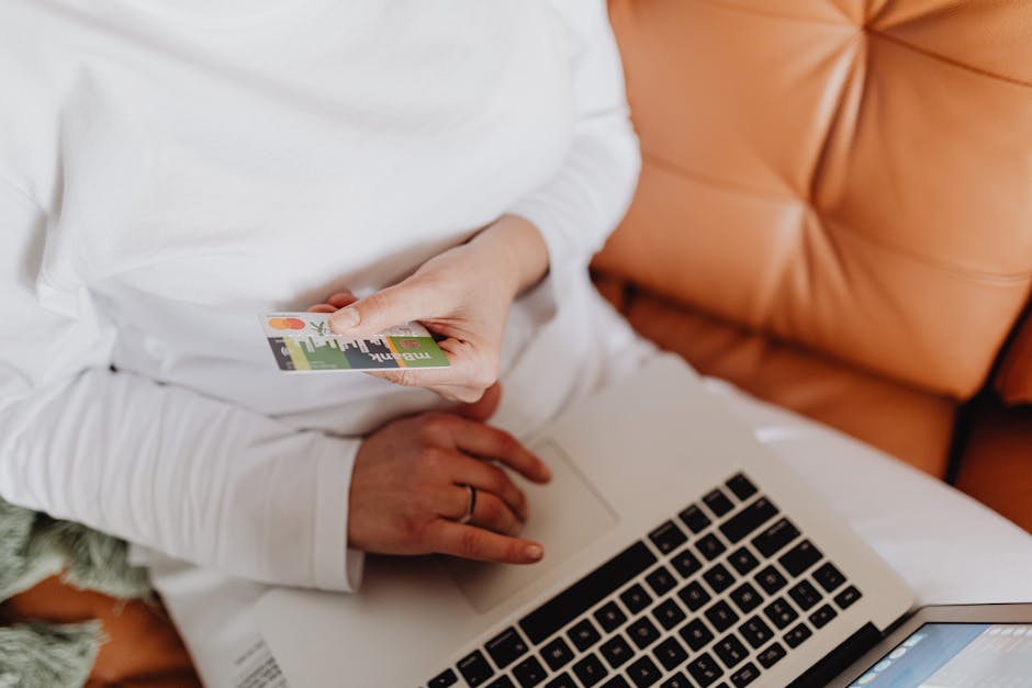 A woman uses a debit card for online shopping on a laptop indoors.