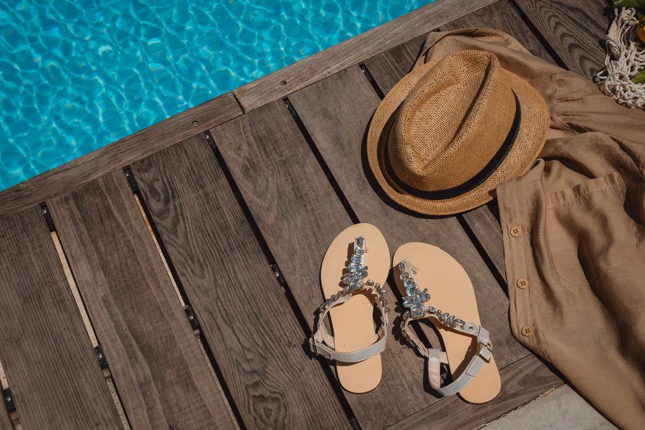Stylish summer gear by the poolside featuring a straw hat and embellished sandals on rustic decking.