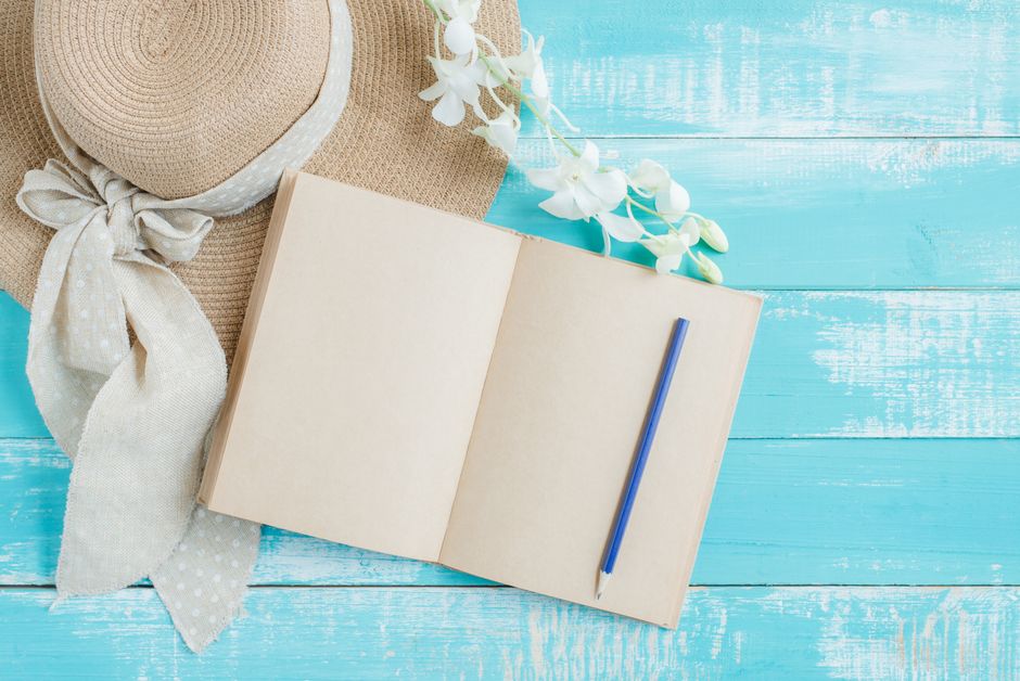 A creative flat lay featuring a straw hat, a blank notebook, and a pencil on a blue wooden surface.