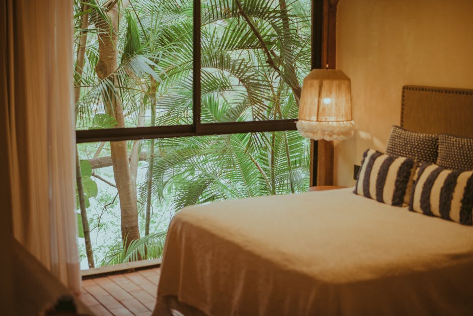 Cozy modern bedroom with a window overlooking tropical vegetation, creating a serene ambiance.