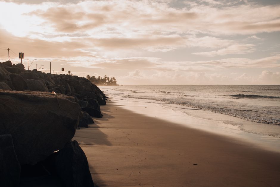 Tranquil beach scene at sunset with gentle waves and rocky shoreline.