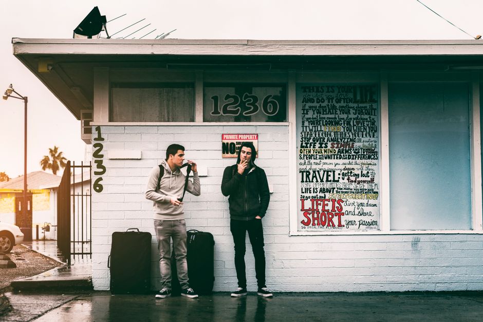 Two young men with luggage and hoodies standing outside a motel in Las Vegas.
