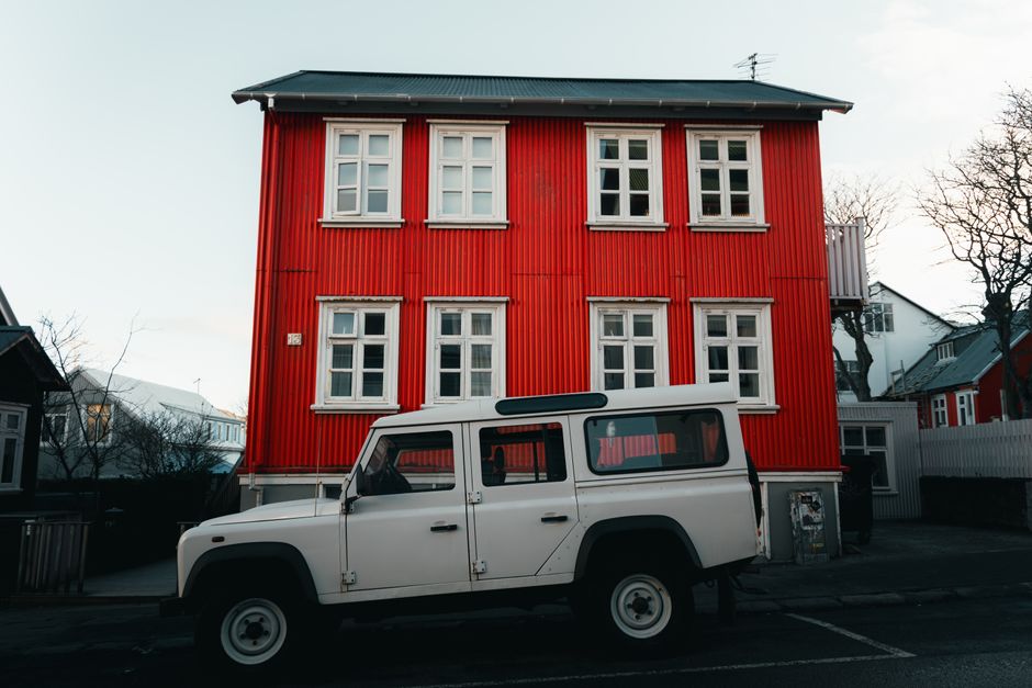 A picturesque red wooden house with a white SUV parked in front in Iceland's winter setting.