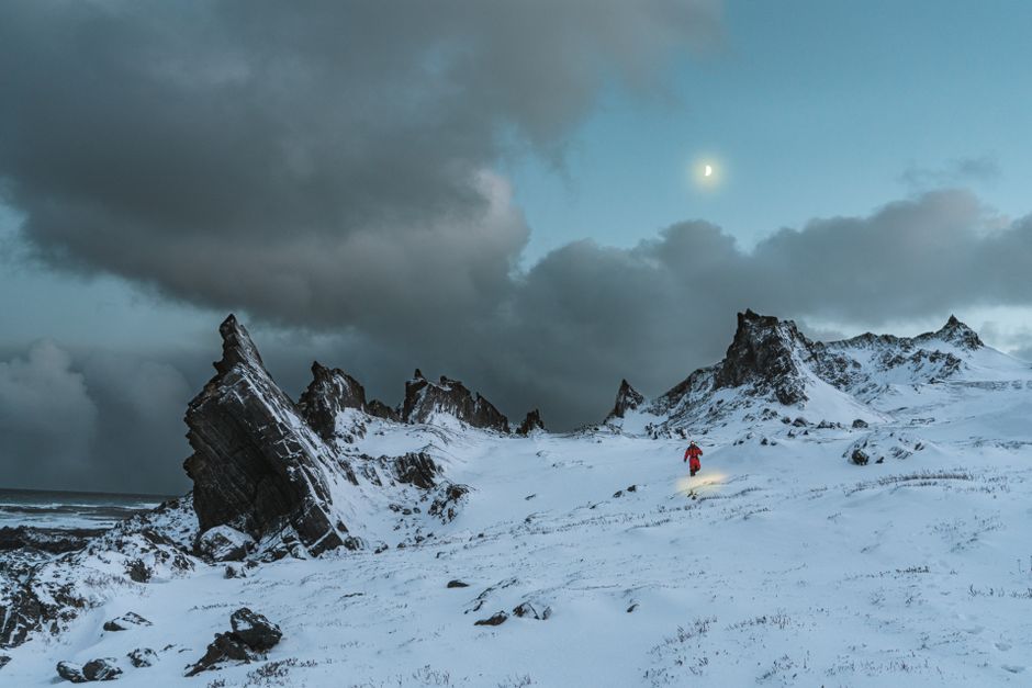 Adventurous hiker traverses snowy mountain terrain under a moody sky.