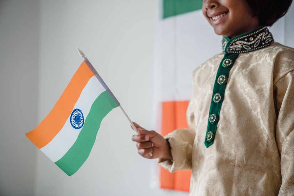 A joyful child in traditional attire holding the Indian flag, celebrating indoors.