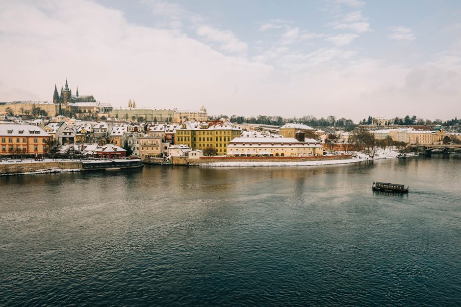 Picturesque winter view of Prague's iconic riverside and architecture under snow.