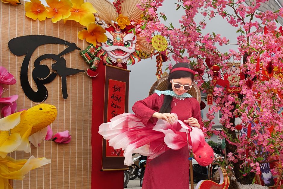 Woman styling pink paper decorations for a festive Lunar New Year setting with vibrant cherry blossoms.