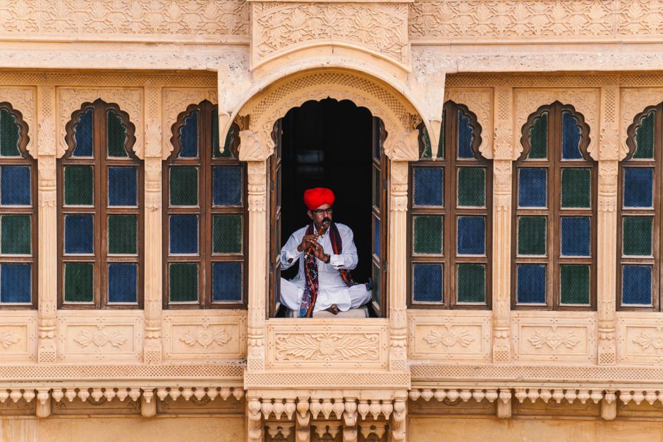 Rajasthani musician playing a flute in a traditional jharokha in Jaisalmer, India.