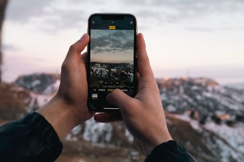 Hands holding a smartphone capturing a stunning snowy mountain vista at dusk.