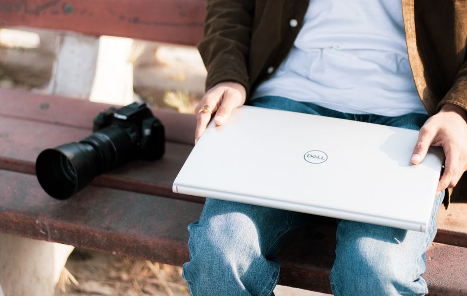 A man seated outdoors with a camera and a laptop on a bench. Perfect for creative workspace themes.
