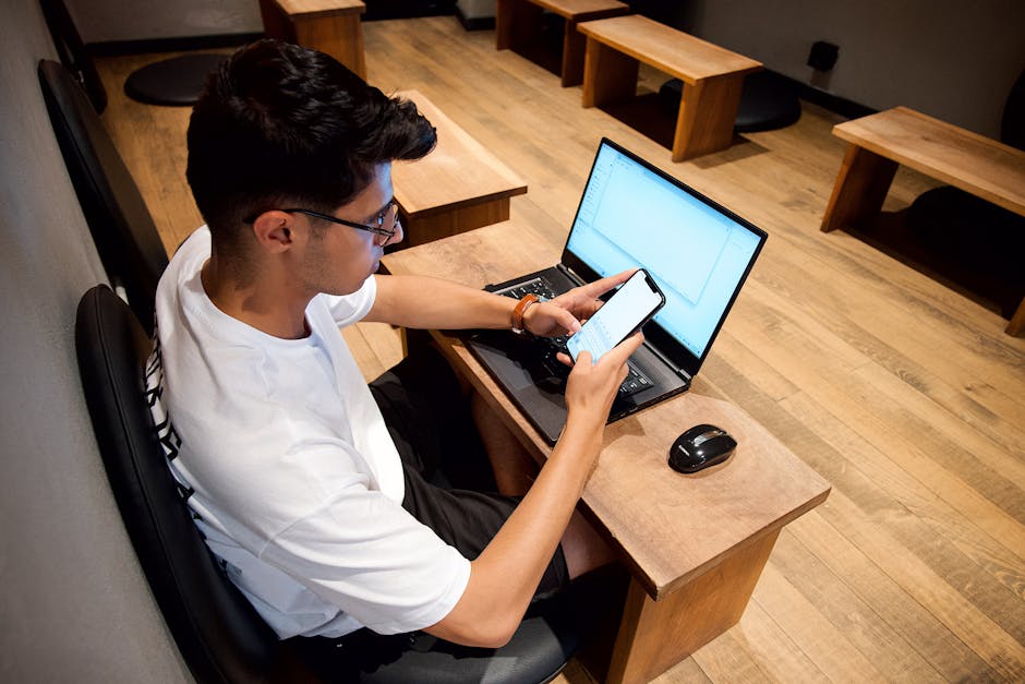 Man multitasking with a laptop and smartphone in a tech-friendly workspace.