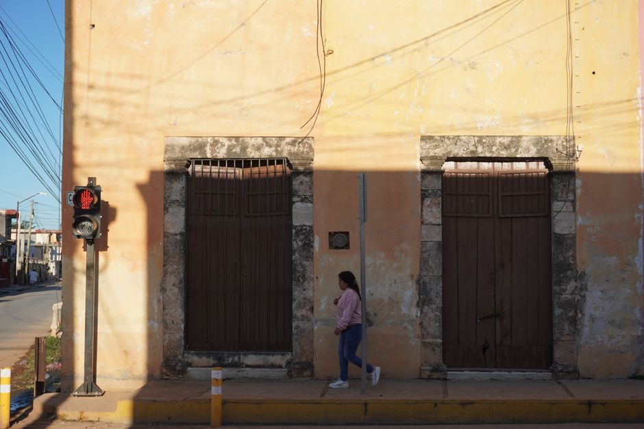 A woman walks past old colonial doors in sunlight, Yucatán.