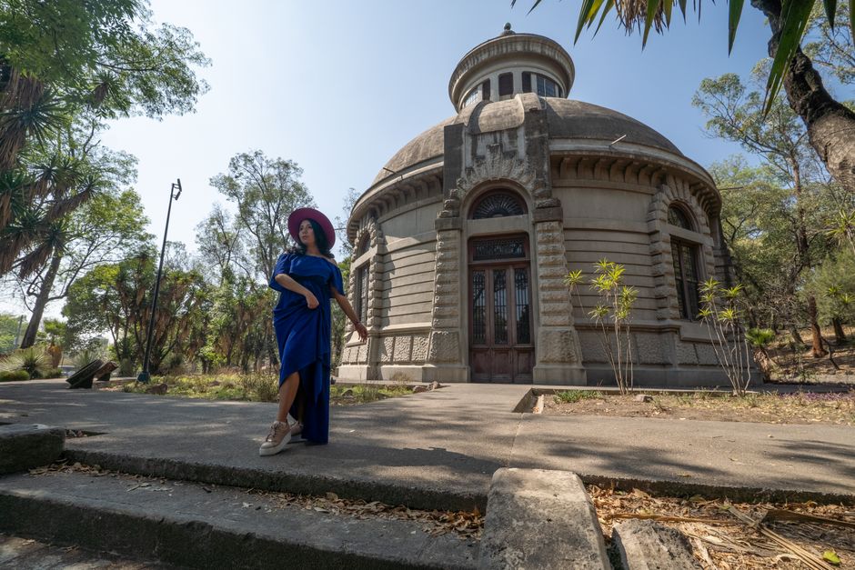 Woman in a blue dress strolling by a historic dome building in a serene park setting in Mexico City.