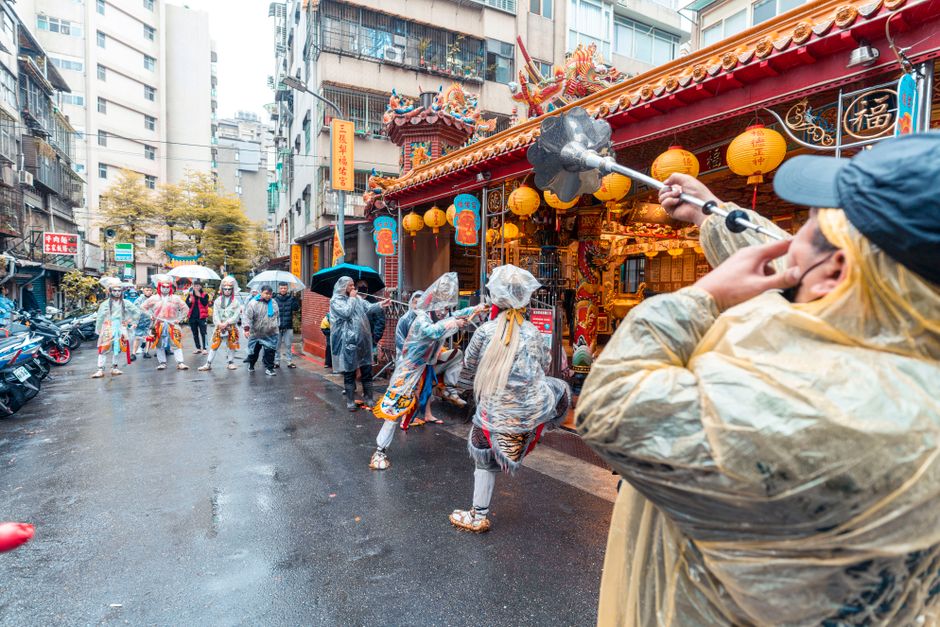 A lively street festival featuring performers in traditional attire and raincoats amidst colorful Chinese lanterns.