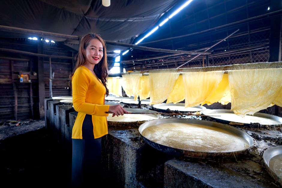 Asian woman prepares rice paper in an indoor Vietnamese workplace.