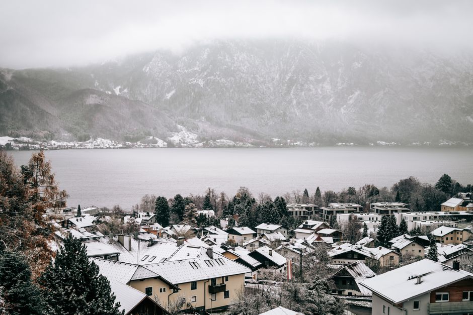 Charming snow-covered alpine village with mountain and lake backdrop, creating a serene winter landscape.